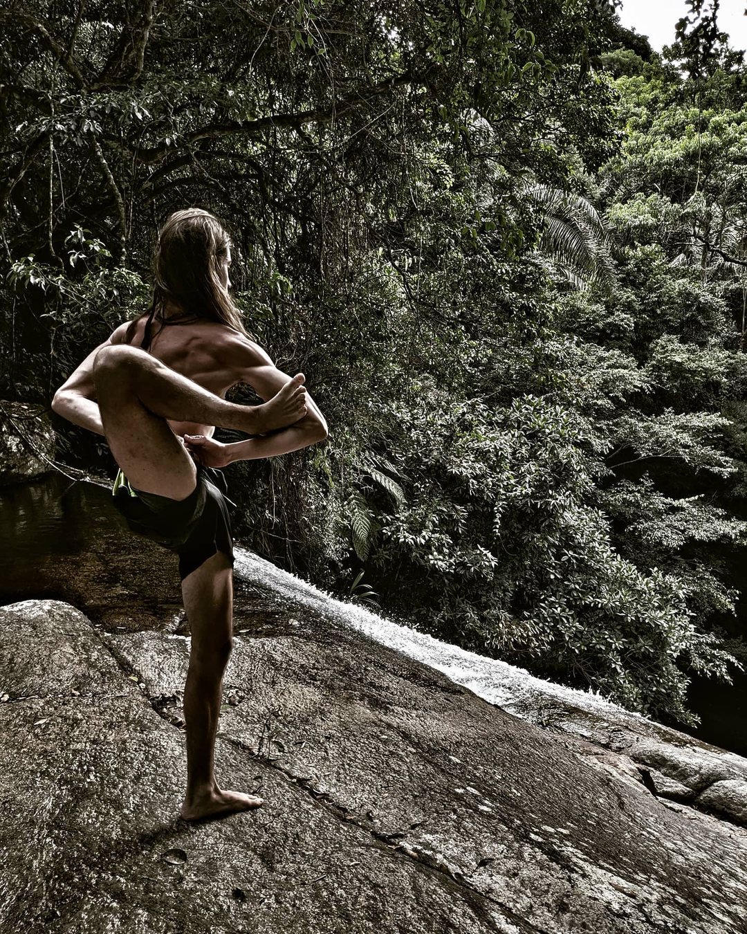 Praticante realiza uma postura avançada de asana sobre a pedra, diante da mata